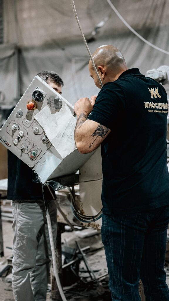 Two workers manage a control panel in an industrial setting, collaborating on machinery.
